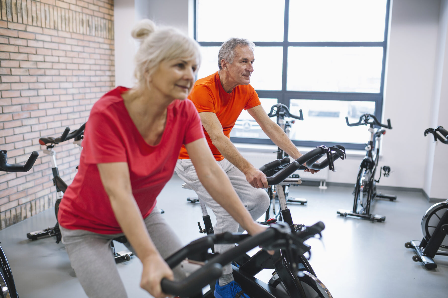 Ouder koppel fietst samen op een spinningfiets in een moderne fitnessruimte.
