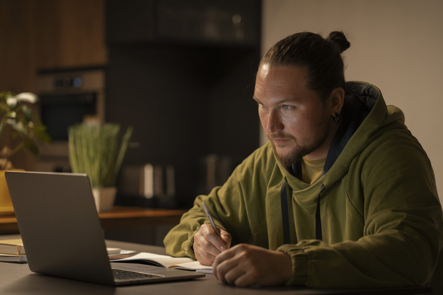 Man maakt 's avonds aantekeningen naast zijn laptop aan de keukentafel.