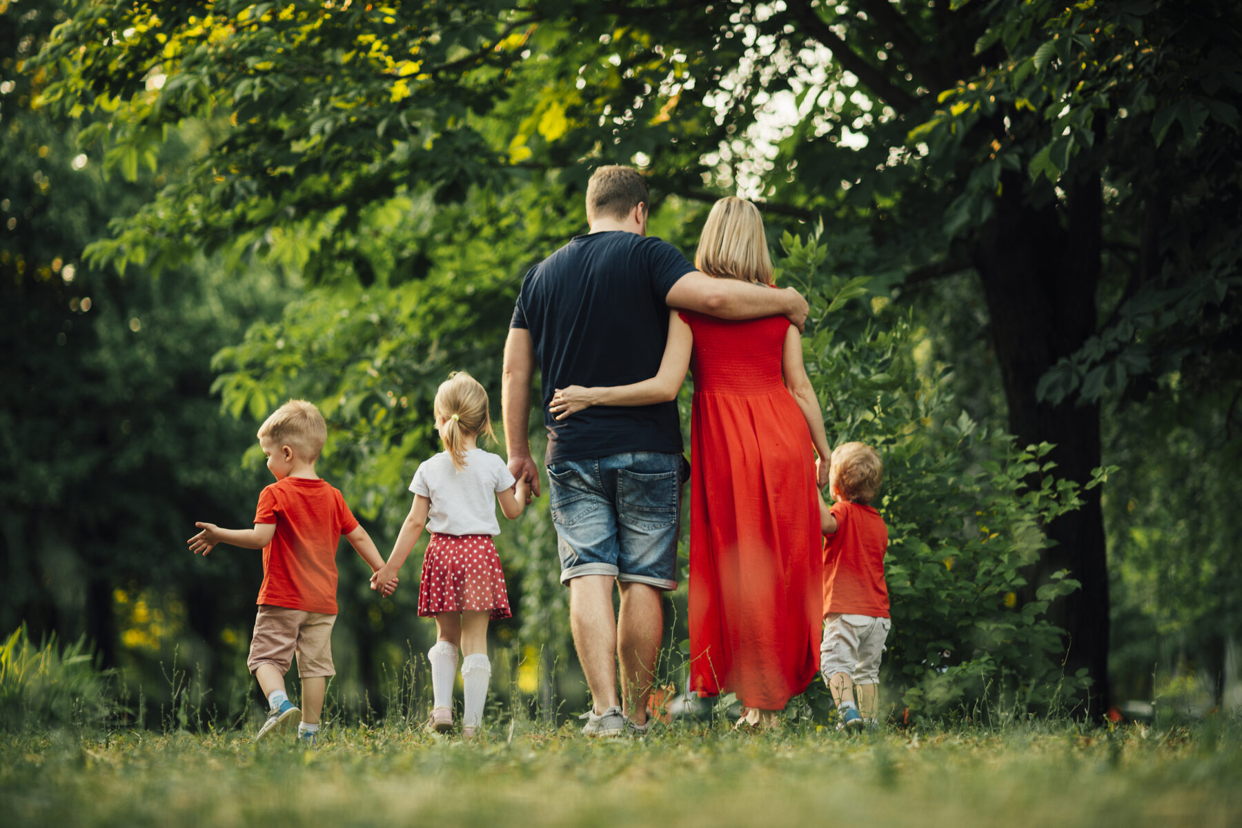 Gezin met kinderen wandelt hand in hand door een groen park.